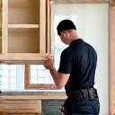 A uniformed installer fitting a new kitchen cabinet.